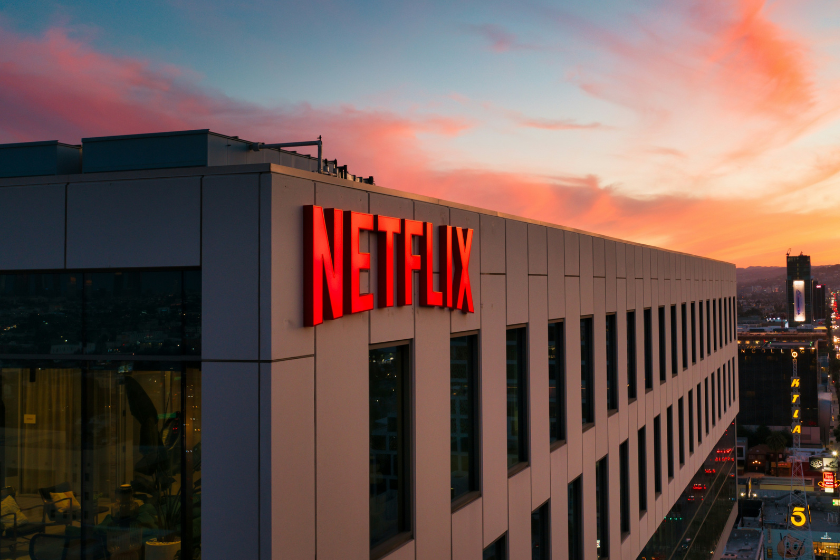 Ein modernes Bürogebäude mit leuchtend rotem Schriftzug "Netflix" an der Fassade. Im Hintergrund ist Abendstimmung in der Stadt zu erahnen.