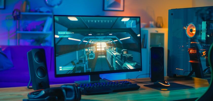 Gaming-Setup mit Monitor, Gaming-PC, Tastatur, Maus und Headset in bunter RGB-Beleuchtung.