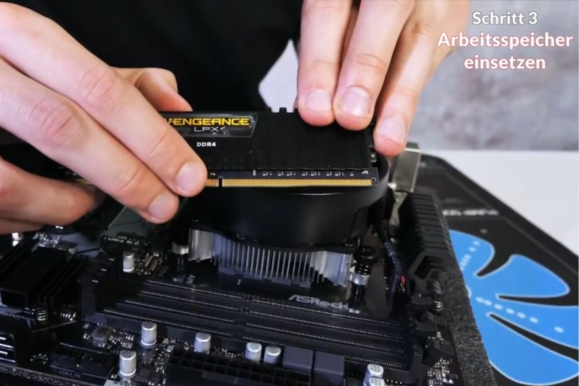 Nahaufnahme einer Person, die einen RAM-Riegel auf einem ASRock-Mainboard einsetzt.