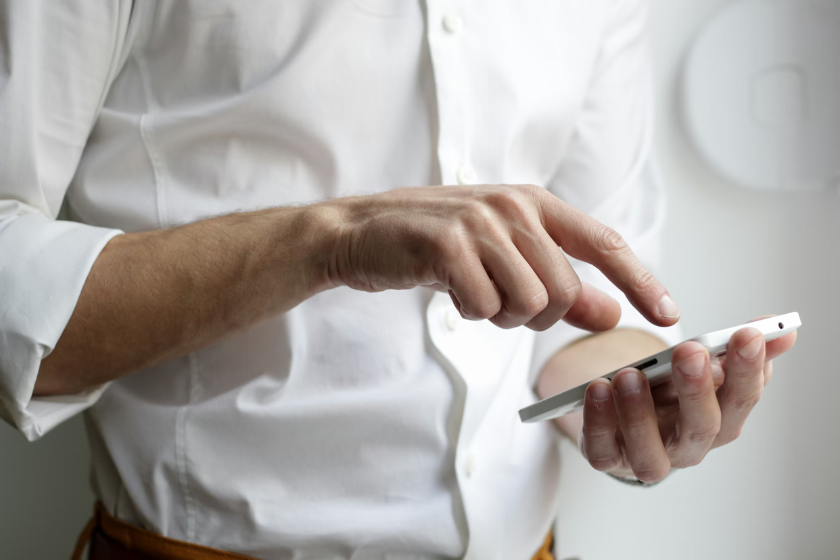 Mann im weißen Hemd hält ein Smartphone in der Hand und tippt auf den Bildschirm.