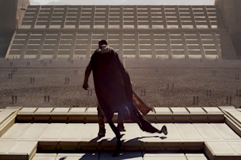 Filmszene: eine monumentale Anlage mit unzähligen militärischen Truppen mit Standarten im Hintergrund. Im Vordergrund zu sehen ist ein Mann mit einem wehenden Umhang, der den aufgereihten Truppen zugewandt auf einer Empore steht.