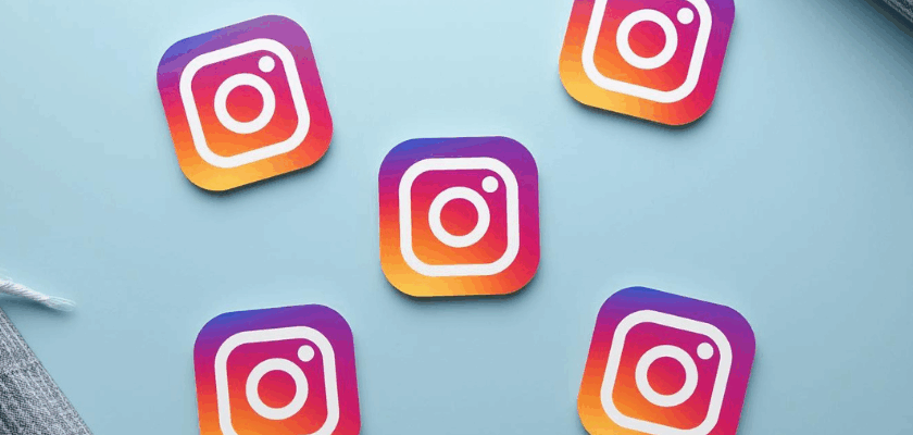 Mehrere Instagram-Logos in bunten Farben auf einem hellblauen Hintergrund, verteilt in einer flachen Anordnung mit dekorativen Stoffelementen am Rand.