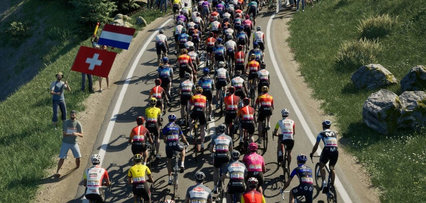 Ein Screenshot aus dem Pro Cycling Manager 25. Zu sehen ist ein dichtes Fahrerfeld eines Radrennens, das auf einer schmalen, kurvigen Straße durch eine grüne Landschaft fährt, während zahlreiche Zuschauer am Straßenrand stehen und Fahnen schwenken. Die Sportler tragen unterschiedliche Teamtrikots und Helme, und das Bild ist aus erhöhter Perspektive aufgenommen, sodass die gesamte Gruppe sowie die umgebende Vegetation gut erkennbar sind.