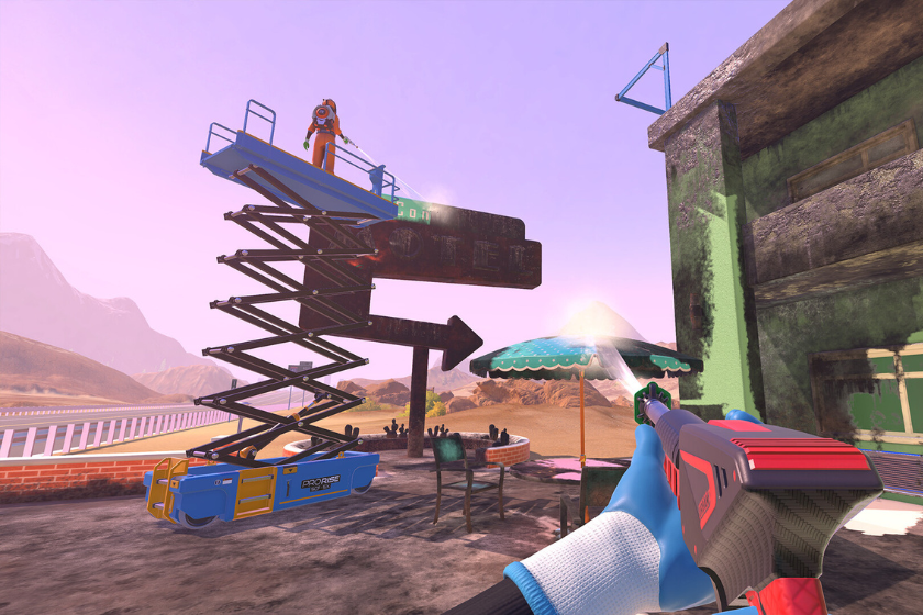 Szene aus PowerWash Simulator 2: Eine Person steht auf einer Hebebühne und reinigt ein großes Schild mit einem Hochdruckreiniger. Im Vordergrund ist die Perspektive aus der Ich-Ansicht mit einem Reinigungsgerät zu sehen, während sich die Szene in einer staubigen Wüstenumgebung mit Gebäuden und Sitzgelegenheiten abspielt.