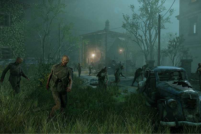 Eine düstere Szene in einem nebligen Dorf: Mehrere Zombies bewegen sich langsam über eine überwucherte Straße in Richtung Kamera. Im Hintergrund steht ein altes Haus mit schwachem Licht in den Fenstern, umgeben von Bäumen und Stromleitungen. Rechts im Vordergrund ist ein verlassenes, verrostetes Auto zu sehen. Die Atmosphäre ist unheimlich und grünlich getönt.