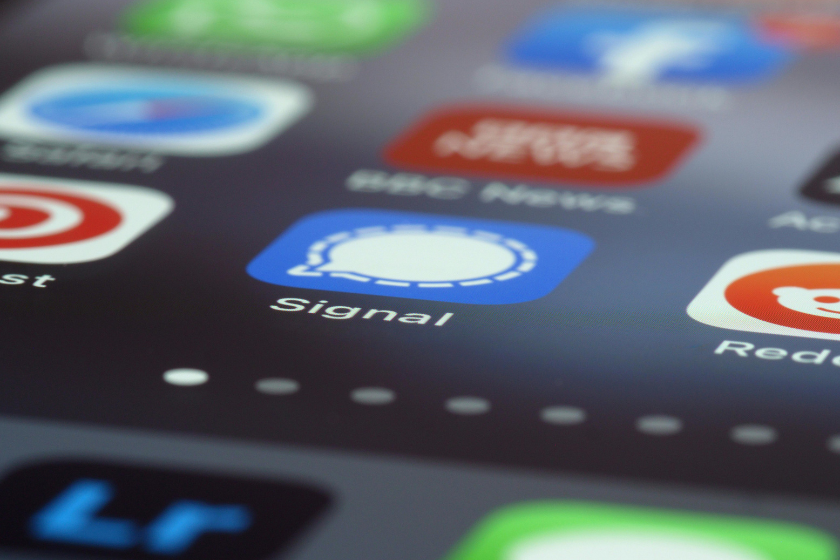 Detailaufnahme eines Smartphone-Displays mit App-Icons, im Fokus die Messaging-App „Signal“ (blaues Symbol mit weißer Sprechblase). Weitere unscharfe App-Icons sind im Hintergrund erkennbar.