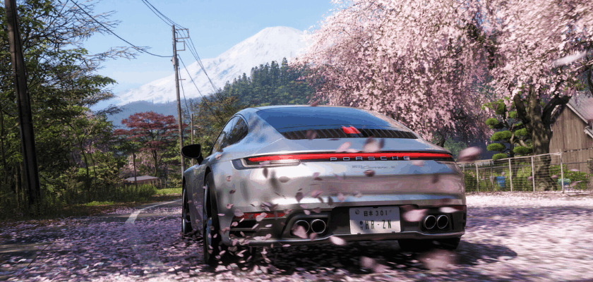 Ein silberner Porsche 911 fährt in Forza Horizon 6 durch eine japanische Landschaft mit blühenden Kirschbäumen. Im Hintergrund erhebt sich ein schneebedeckter Berg, während Blütenblätter über die Straße wehen.