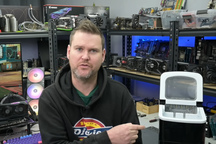 YouTuber TrashBench sitzt in seiner Werkstatt vor mehreren Computerkomponenten und zeigt auf eine Eiswürfelmaschine. Das Gerät wurde in einem Experiment zur Kühlung einer Nvidia GeForce RTX 3060 eingesetzt. Im Hintergrund sind Grafikkarten, Mainboards und ein Testsystem zu sehen.