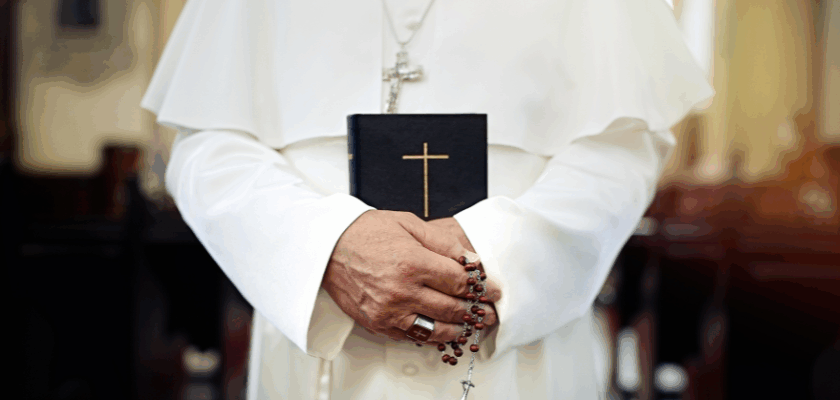 Nahaufnahme einer Person in weißer Papst-Kleidung, die in einer Kirche eine Bibel mit goldenem Kreuz sowie einen Rosenkranz in den Händen hält. Das Bild dient als Symbol für die offizielle Gebets-App des Papstes und die bekannt gewordene Sicherheitslücke.