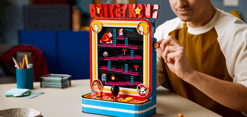 Eine Person hält ein LEGO-Fass neben dem LEGO Super Mario Donkey Kong Arcade-Set, das den klassischen Spielautomaten mit Jumpman, Donkey Kong und beweglichen Spielelementen detailgetreu nachbildet.