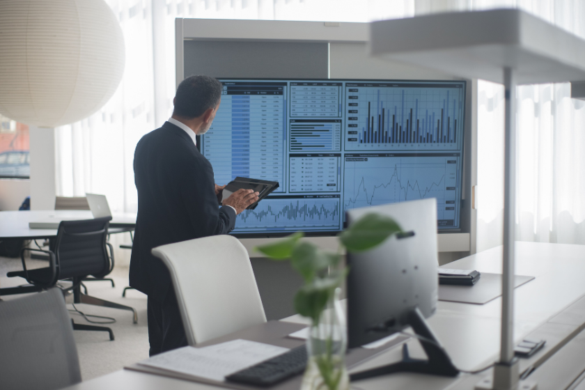 Person analysiert Finanzdaten und Diagramme auf einem großen Bildschirm in einem modernen Büro.