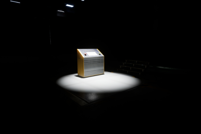 Das Bild zeigt eine Spielszene aus „The Cabin Factory“. Im Mittelpunkt steht ein beleuchtetes Bedienpult, das in einer ansonsten dunklen Halle unter einem einzelnen Scheinwerfer steht. Die minimalistische Inszenierung und die tiefen Schatten erzeugen eine geheimnisvolle, beklemmende Atmosphäre. Das Motiv zeigt einen der Titel aus dem aktuellen Liminal Spaces Humble Bundle.