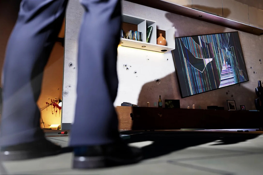 Das Bild zeigt eine Spielszene aus Vampire: The Masquerade – Swansong. Im Vordergrund sind die Beine einer Person zu sehen, während im Hintergrund ein verwüstetes Wohnzimmer mit Einschusslöchern in der Wand, Blutflecken und einem beschädigten Fernseher zu erkennen ist.