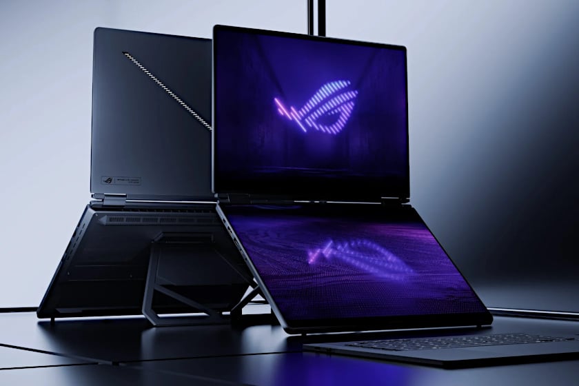 Produktfoto des ASUS ROG Zephyrus Duo zeigt das aufgeklappte Dual-Screen-Gaming-Notebook mit dem leuchtenden ROG-Logo auf lila-blauem Hintergrund auf beiden Bildschirmen. Im Hintergrund ist ein weiteres, zugeklapptes Laptop-Modell in Grau zu sehen, während das Gerät im Vordergrund auf einer schwarz spiegelnden Oberfläche vor neutralem, hellgrauem Studiohintergrund steht.