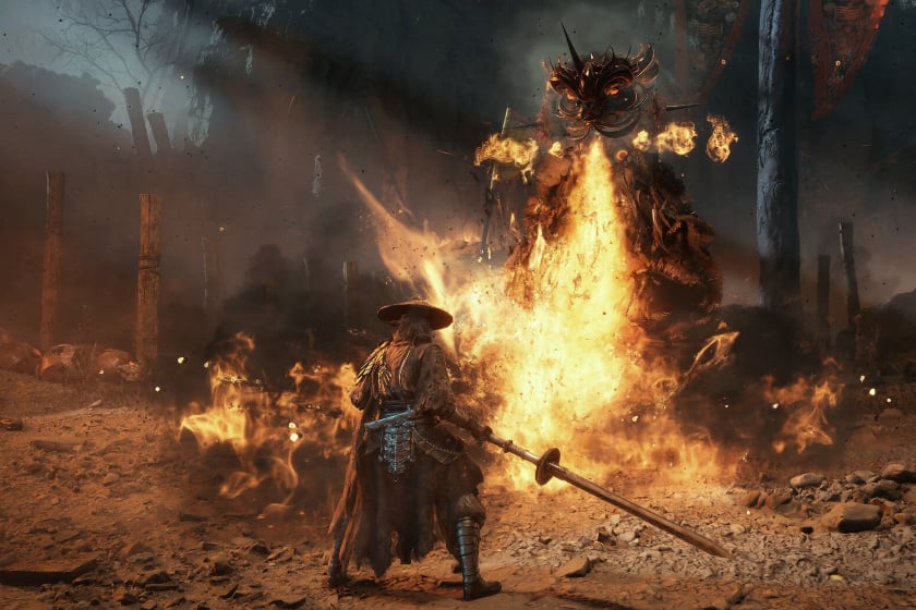 Key-Art zum Videospiel „Phantom Blade Zero" zeigt einen Krieger mit breitkrempigem Hut und langer Speerwaffe, der einem gigantischen, dämonenartigen Wesen aus lodernden Flammen gegenübersteht. Die von Feuer und Rauch durchzogene Schlachtszenerie wird von zerstörten Holzpfählen und roten Bannerfahnen im Hintergrund gerahmt, während funkelnde Glutpartikel durch die Luft wirbeln.