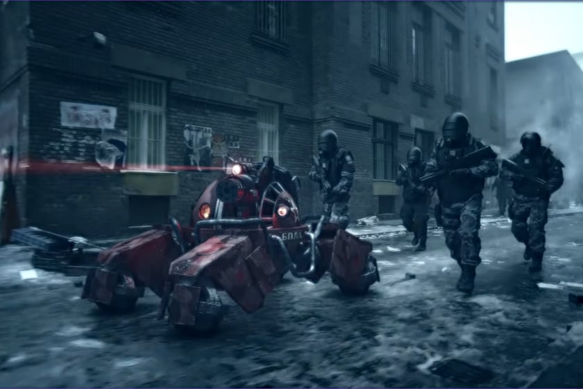 Screenshot aus dem Videospiel „Tom Clancy's Ghost Recon: Future Soldier" zeigt vier schwer bewaffnete Soldaten in taktischer Ausrüstung, die durch eine verschneite, zerstörte Stadtstraße vorrücken. Neben ihnen bewegt sich ein bewaffneter, rot leuchtender Militärroboter mit mehreren Beinen, während im Hintergrund heruntergekommene Häuserfassaden und aufsteigender Rauch die düstere Kriegsatmosphäre unterstreichen.