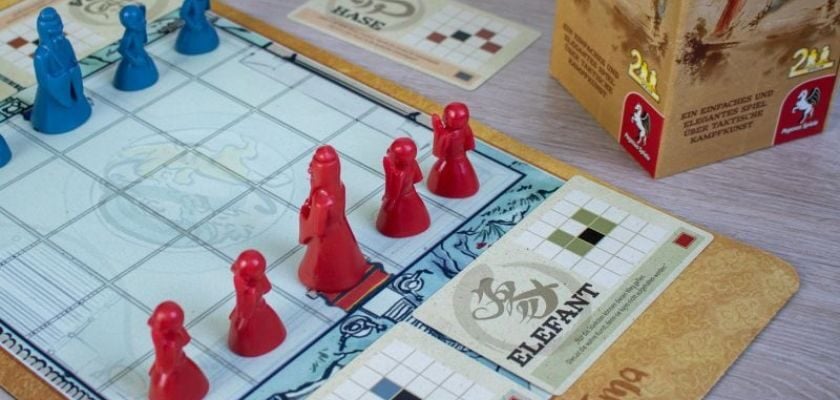 Pegasus Onitama Brettspiel mit roten und blauen Spielfiguren sowie Bewegungskarten auf dem Spielbrett.