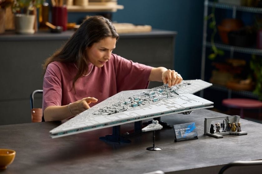 Frau baut den LEGO Star Wars UCS Executor Supersternzerstörer (75457) auf einem Tisch zusammen. Daneben stehen mehrere Star-Wars-Minifiguren sowie ein kleines Raumschiff-Modell.
