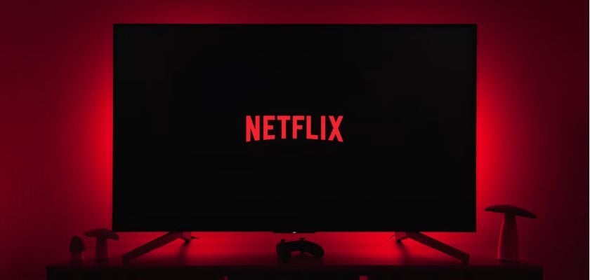 Fernseher mit Netflix-Logo auf schwarzem Bildschirm vor rot beleuchteter Wand.