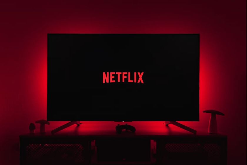 Fernseher mit Netflix-Logo auf schwarzem Bildschirm vor rot beleuchteter Wand.