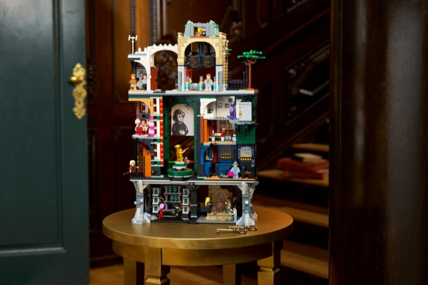 Ein mehrstöckiges LEGO-Modell des Zaubereiministeriums mit offen dargestellten Innenräumen steht auf einem runden Holztisch in einem Innenraum mit Holzvertäfelung und einer Treppe im Hintergrund.