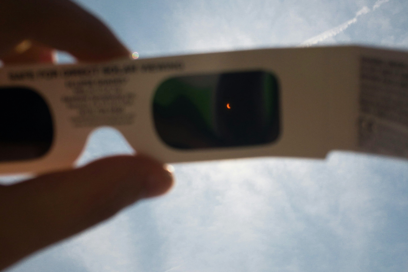 Das Bild zeigt eine Sonnenfinsternis, die durch eine spezielle Schutzbrille beobachtet wird. Die teilweise verdeckte Sonne ist durch das Filterglas als schmale leuchtende Sichel zu erkennen.