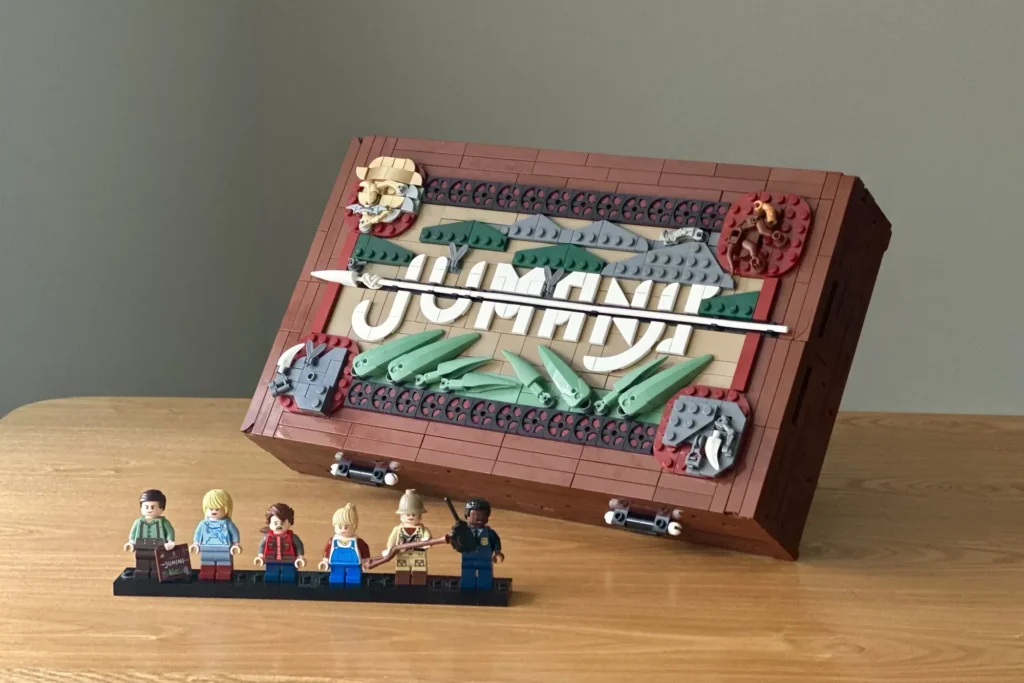 Das Bild zeigt einen Fan-Entwurf für LEGO Ideas in Form des Brettspiels Jumanji. Neben dem aufklappbaren Spielbrett aus LEGO sind sechs Minifiguren der Charaktere auf einer Präsentationsplatte zu sehen.