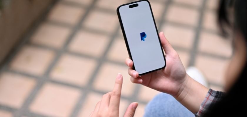Person hält ein Smartphone mit geöffnetem PayPal-Logo auf dem Display in der Hand.
