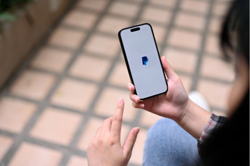 Person hält ein Smartphone mit geöffnetem PayPal-Logo auf dem Display in der Hand.
