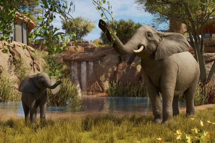 Afrikanischer Elefant mit Jungtier in einem begrünten Gehege mit Wasserstelle in Planet Zoo 2