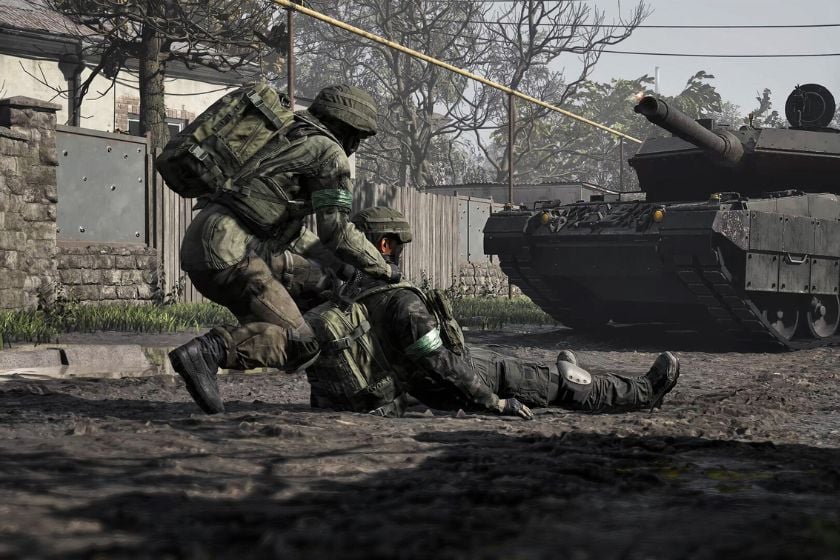 Ein Soldat hilft einem verwundeten Teamkollegen in WARDOGS auf, während im Hintergrund ein Panzer steht.
