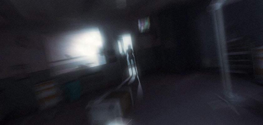 Eine schemenhafte Gestalt steht in einem dunklen, verschwommenen Flur in F.E.A.R. 2: Project Origin.