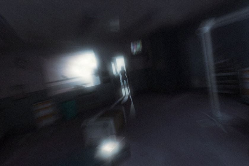Eine schemenhafte Gestalt steht in einem dunklen, verschwommenen Flur in F.E.A.R. 2: Project Origin.