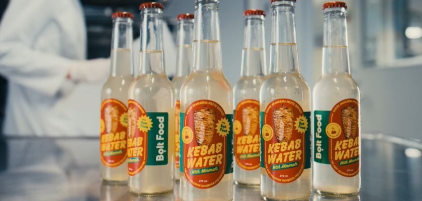 Mehrere Glasflaschen mit der Aufschrift „Kebab Water“ und dem Bolt-Food-Logo stehen auf einer reflektierenden Arbeitsfläche.