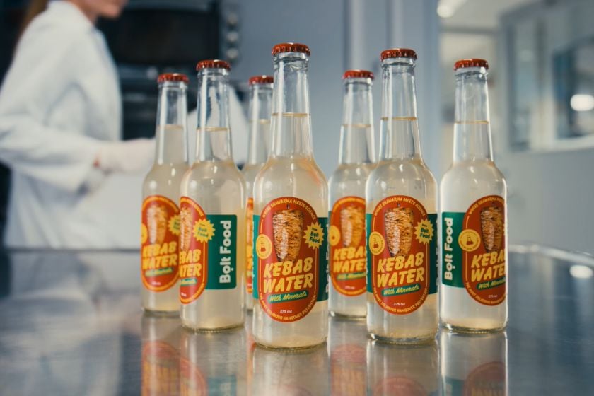 Mehrere Glasflaschen mit der Aufschrift „Kebab Water“ und dem Bolt-Food-Logo stehen auf einer reflektierenden Arbeitsfläche.