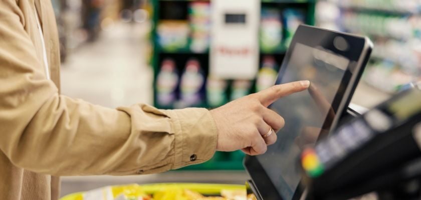 Hand bedient den Touchscreen einer Selbstbedienungskasse in einem Supermarkt.