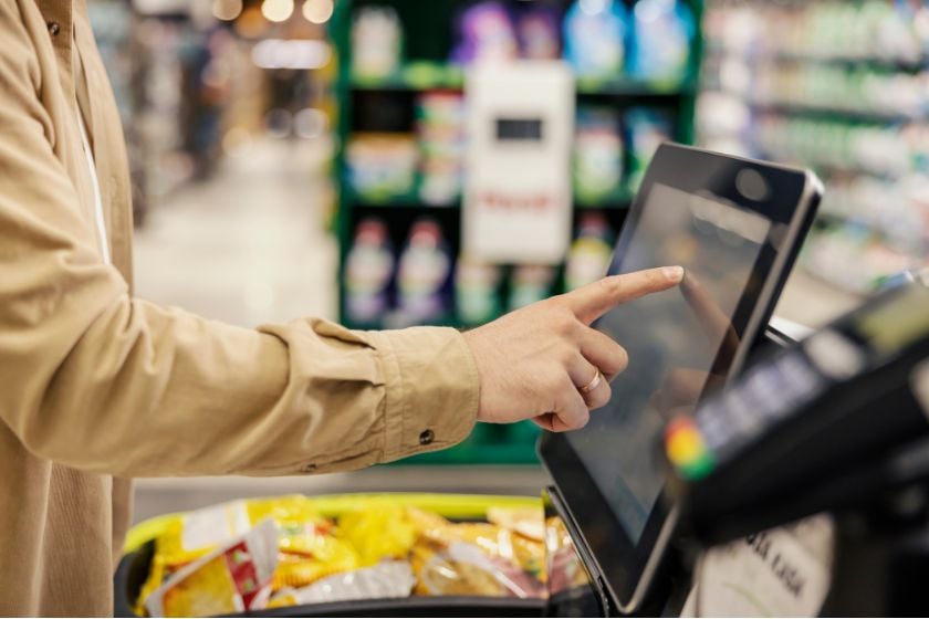 Hand bedient den Touchscreen einer Selbstbedienungskasse in einem Supermarkt.